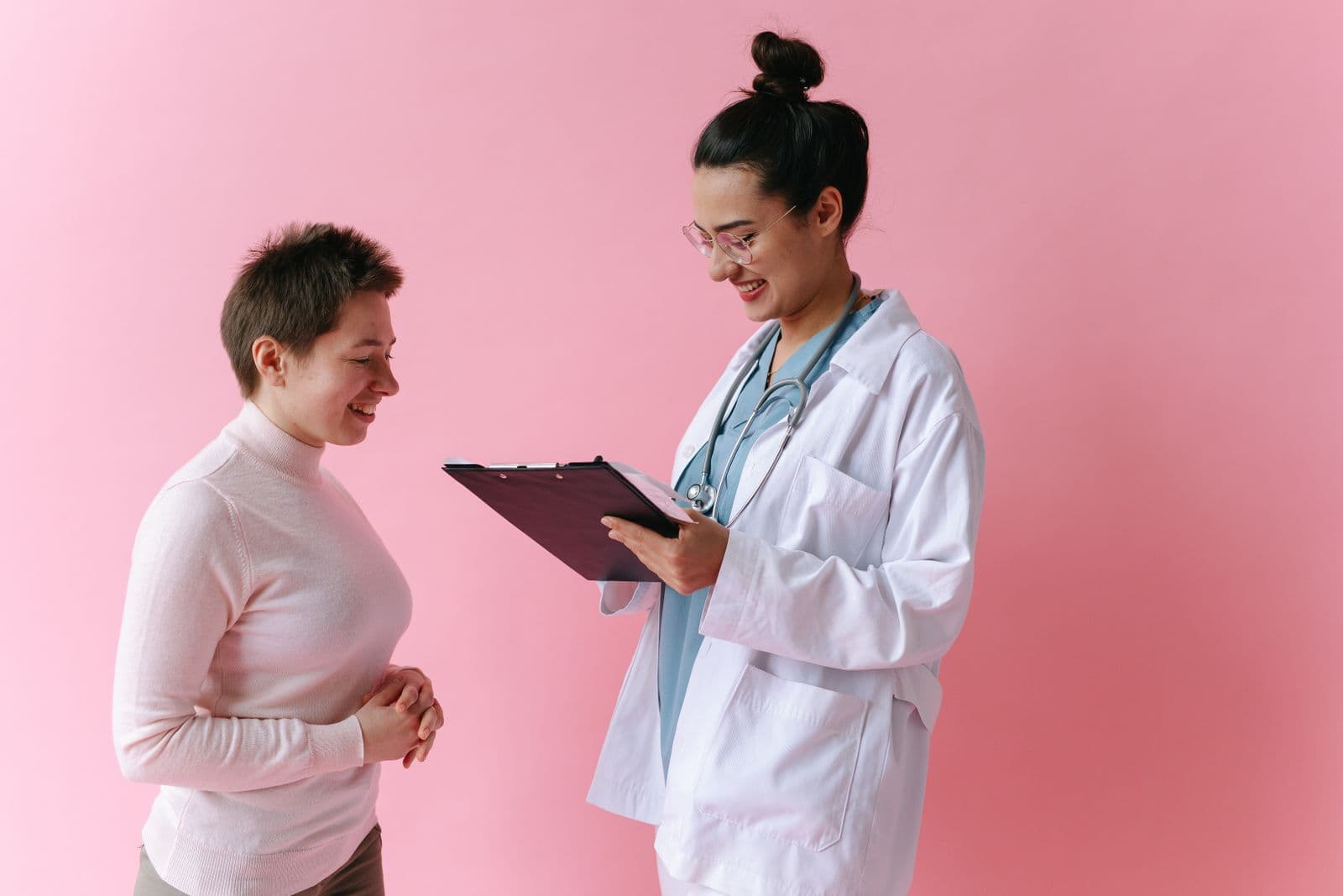 A smiling clinician reviews a clipboard with a patient during a consultation.
